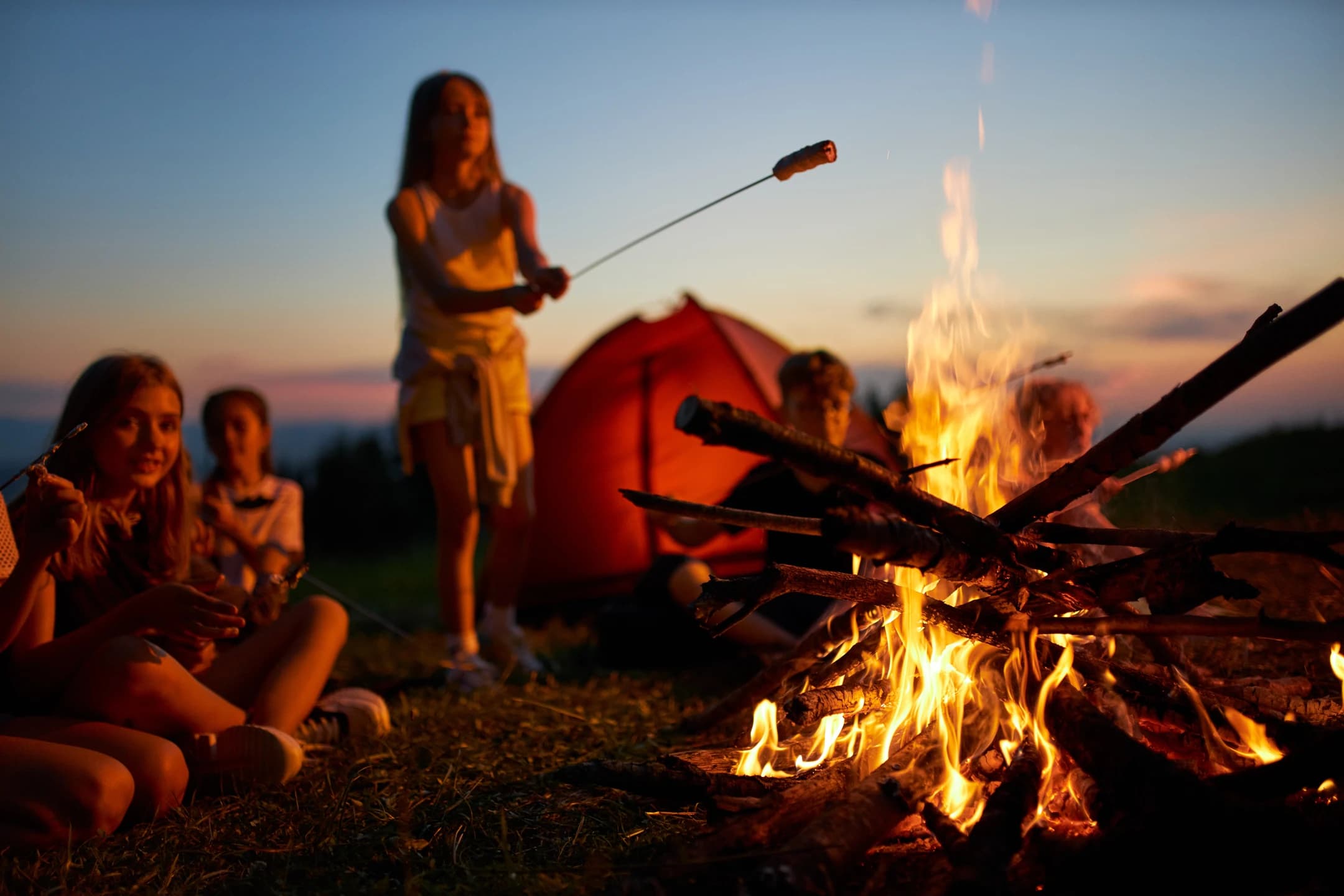 Children roasting marshmallows around a campfire at summer camp evening